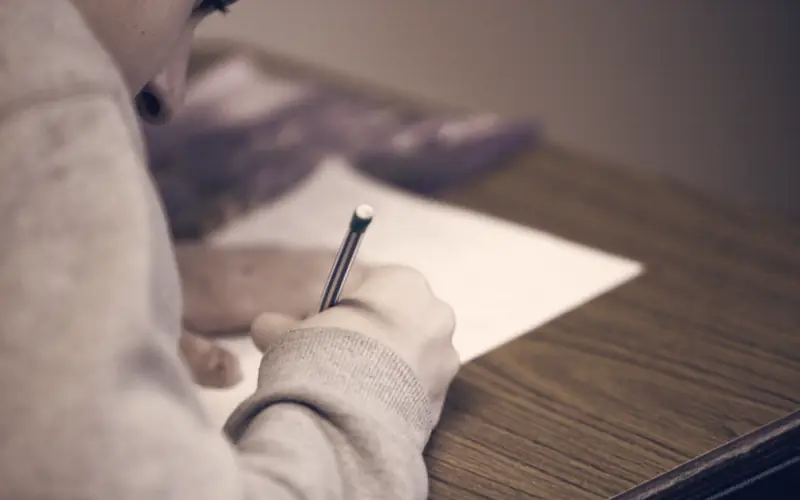 Test taker writing answers on paper with a pencil at a desk