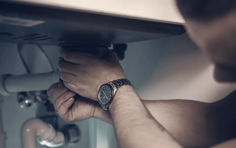 Plumber tightening a pipe fitting under a sink